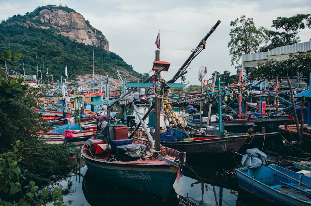 Colorful fishing boats docked under a picturesque rocky mountain backdrop, showcasing a bustling harbor scene.