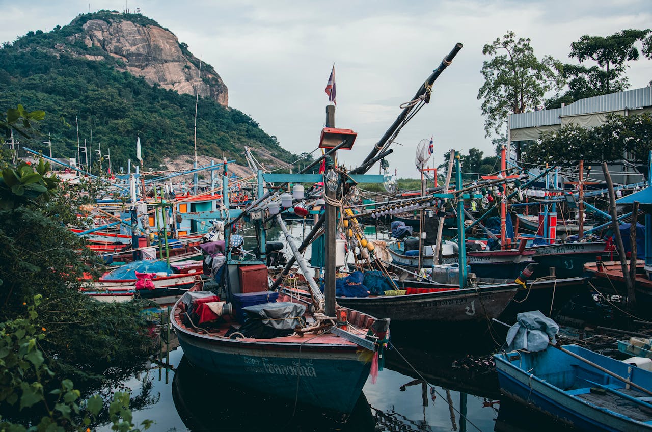 Colorful fishing boats docked under a picturesque rocky mountain backdrop, showcasing a bustling harbor scene.