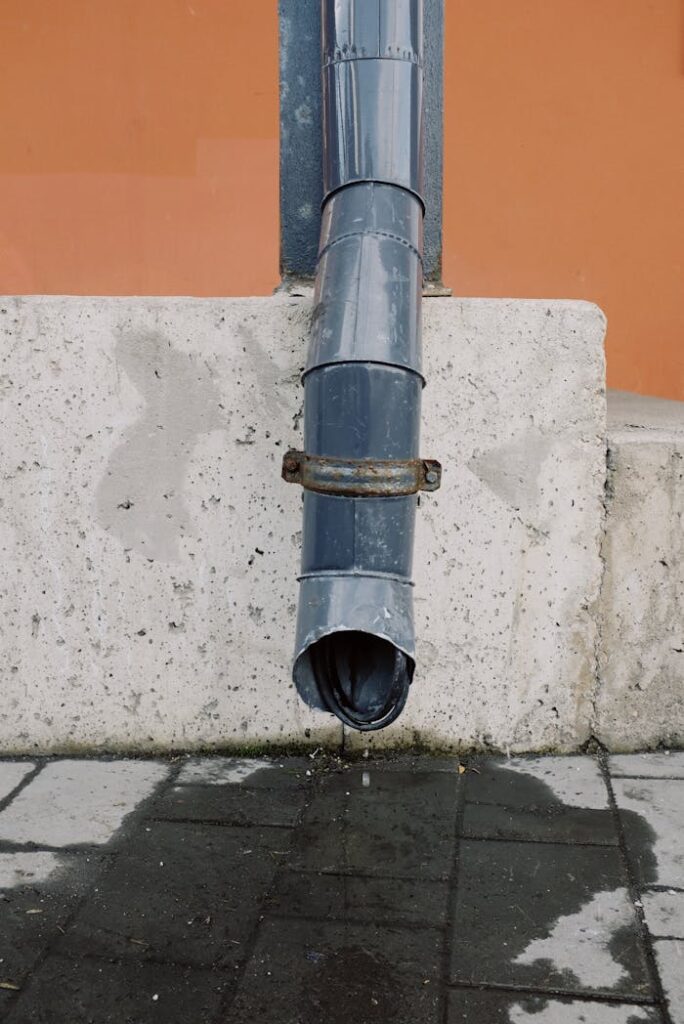 A close-up image of a metal drainage pipe on a concrete wall with visible water runoff.