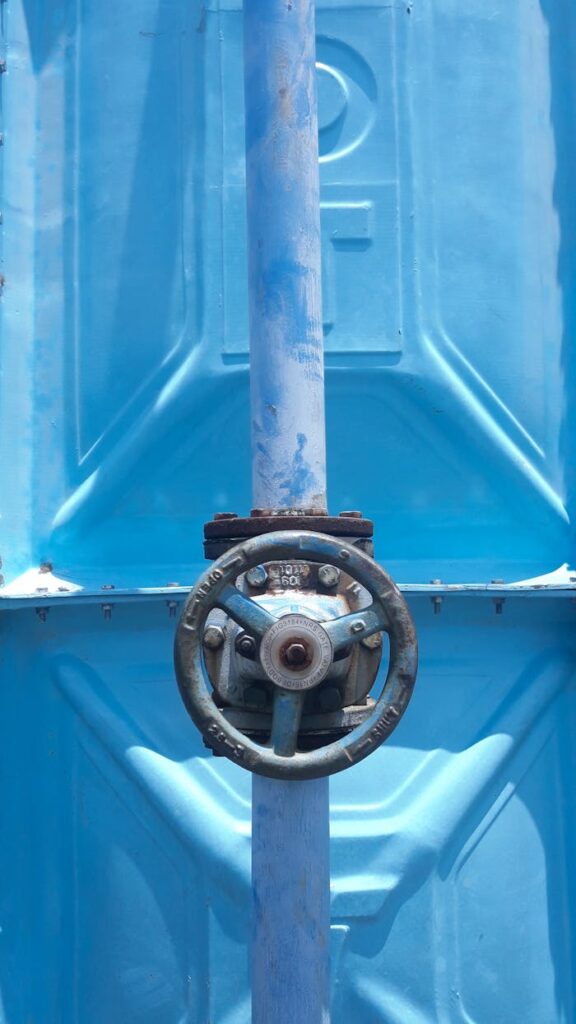 Close-up of a rusty valve on a blue industrial pipe outdoors in daylight.